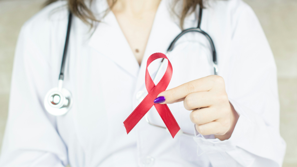 Médico con bata y estetoscopio sosteniendo un lazo rojo que simbiliza los temas de VIH
