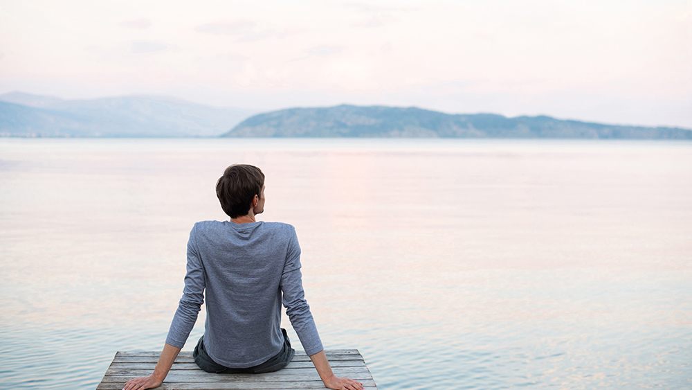 Vista de españda de un hombre sentado tranquilamente frente a un lago